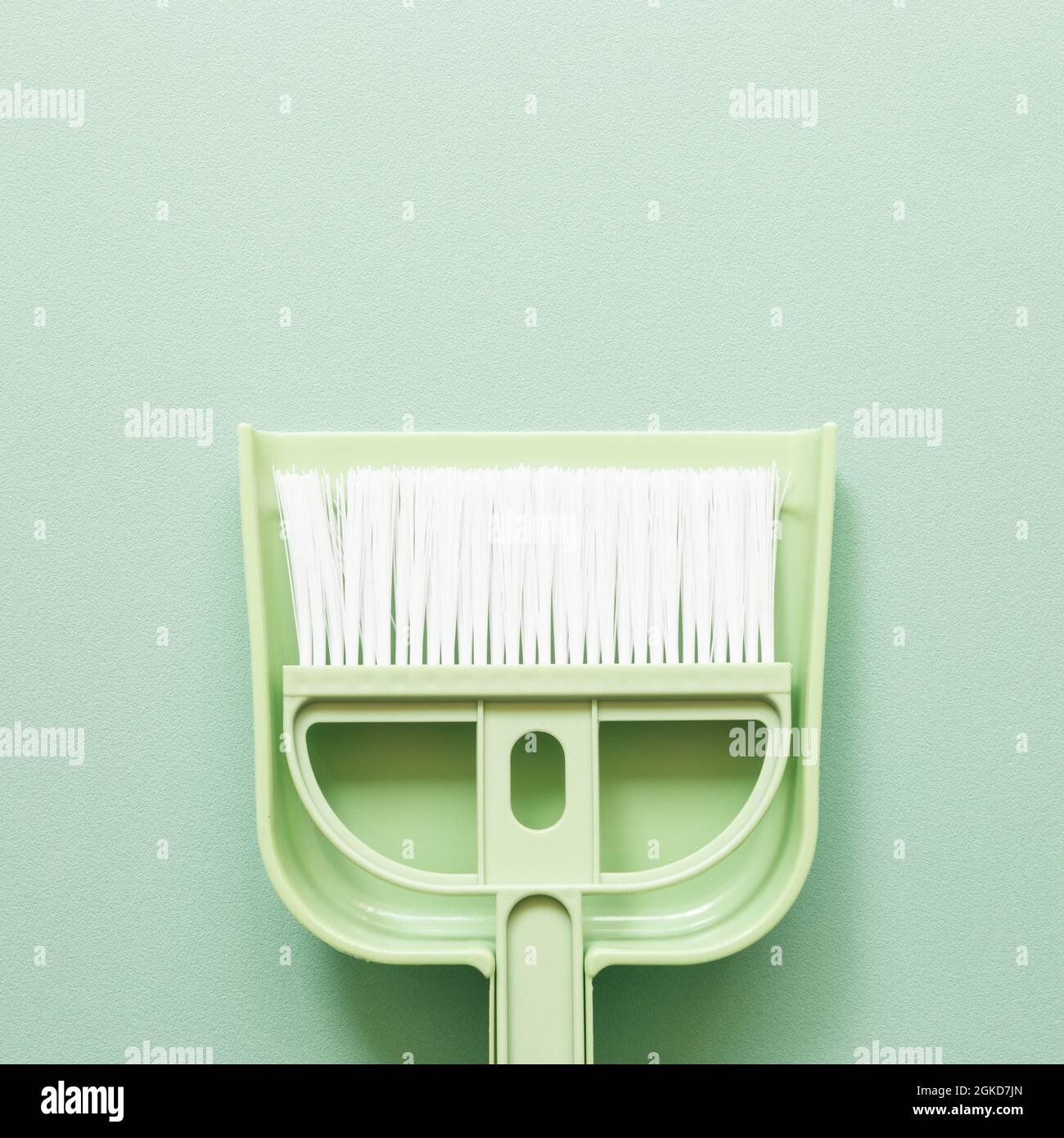 Green broom and dustpan on green background. Cleaning housework concept