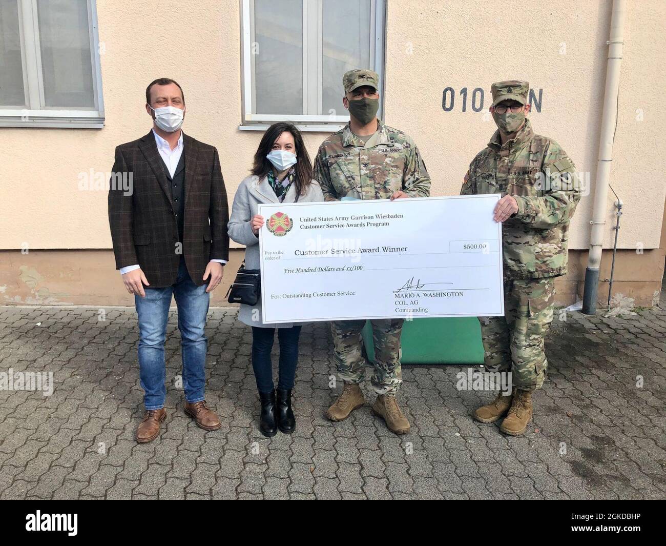 WIESBADEN, Germany -- Julie A. Kelly, education services specialist, receives her check from Col. Mario Washington, garrison commander, Command Sgt. Maj. Christopher Truchon and Scott Mowry, deputy to the garrison commander, for outstanding customer service at U.S. Army Garrison Wiesbaden March 19, 2021. Stock Photo