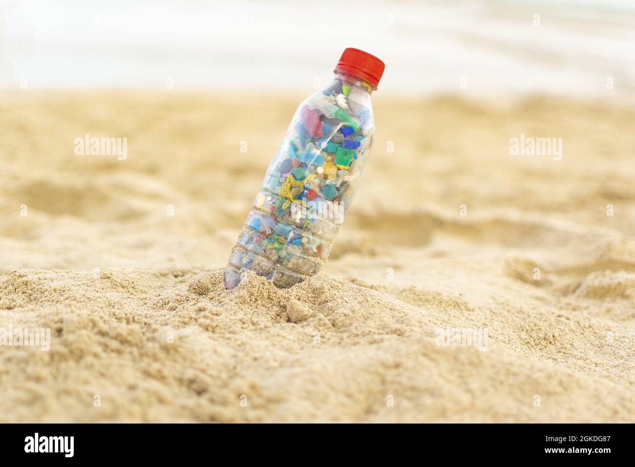 Bottle filled with microplastics lying on the sand of the beach Stock