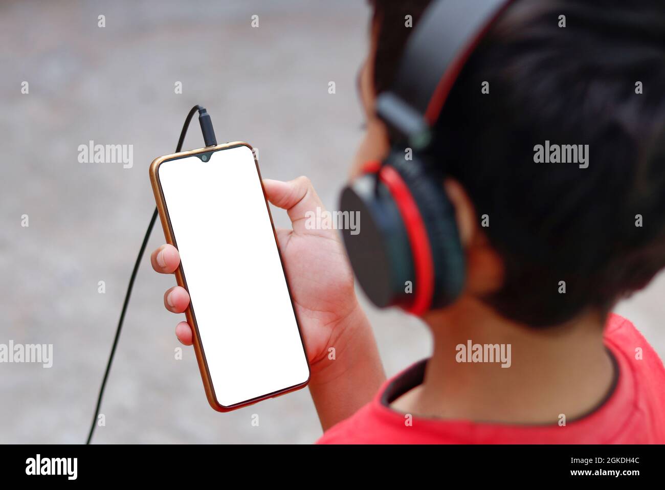Child wearing headphones showing and using blank phone screen outdoors. Stock Photo