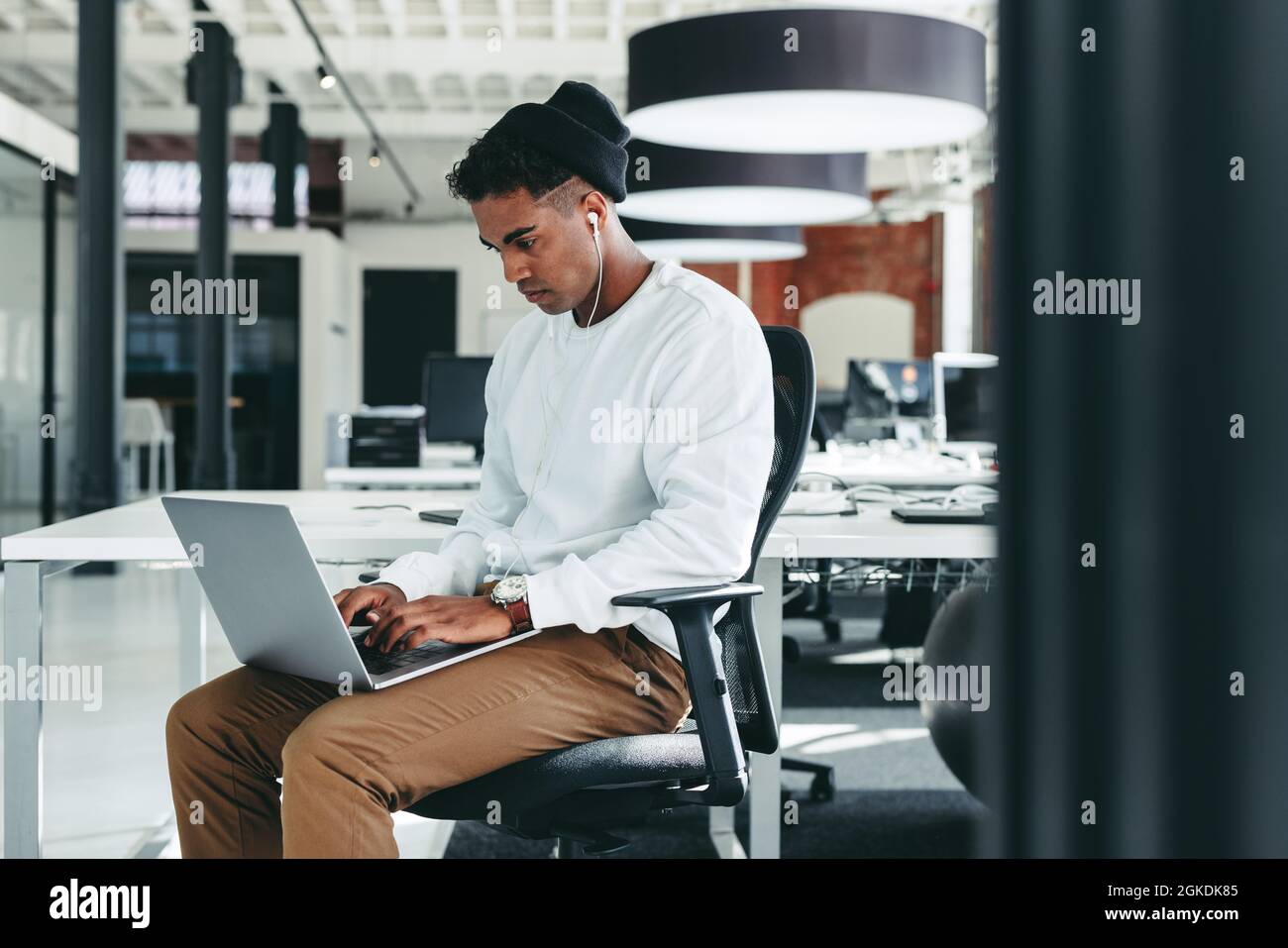 Male programmer working on a new project in an office. Focused young businessman using a laptop while sitting alone in a modern workplace. Young softw Stock Photo