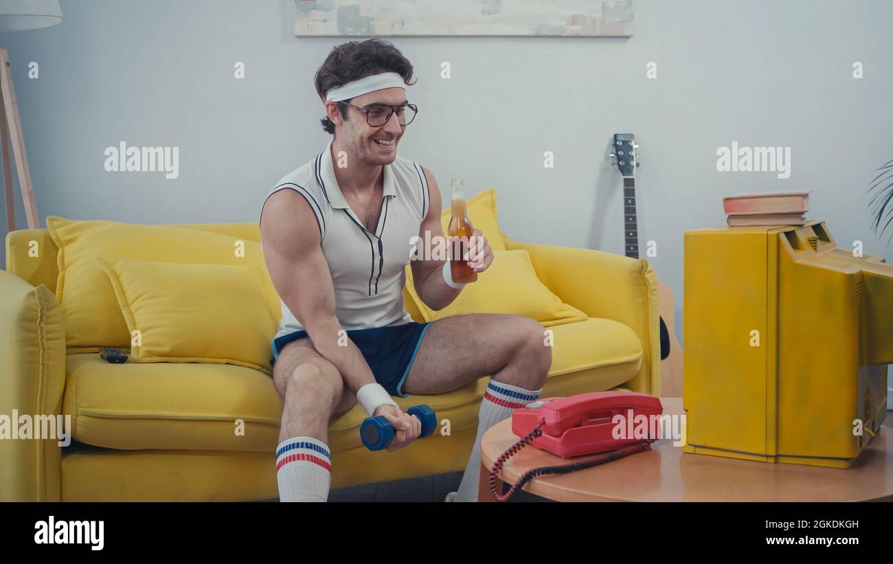 happy sportsman holding glass bottle of beer and lifting dumbbell while