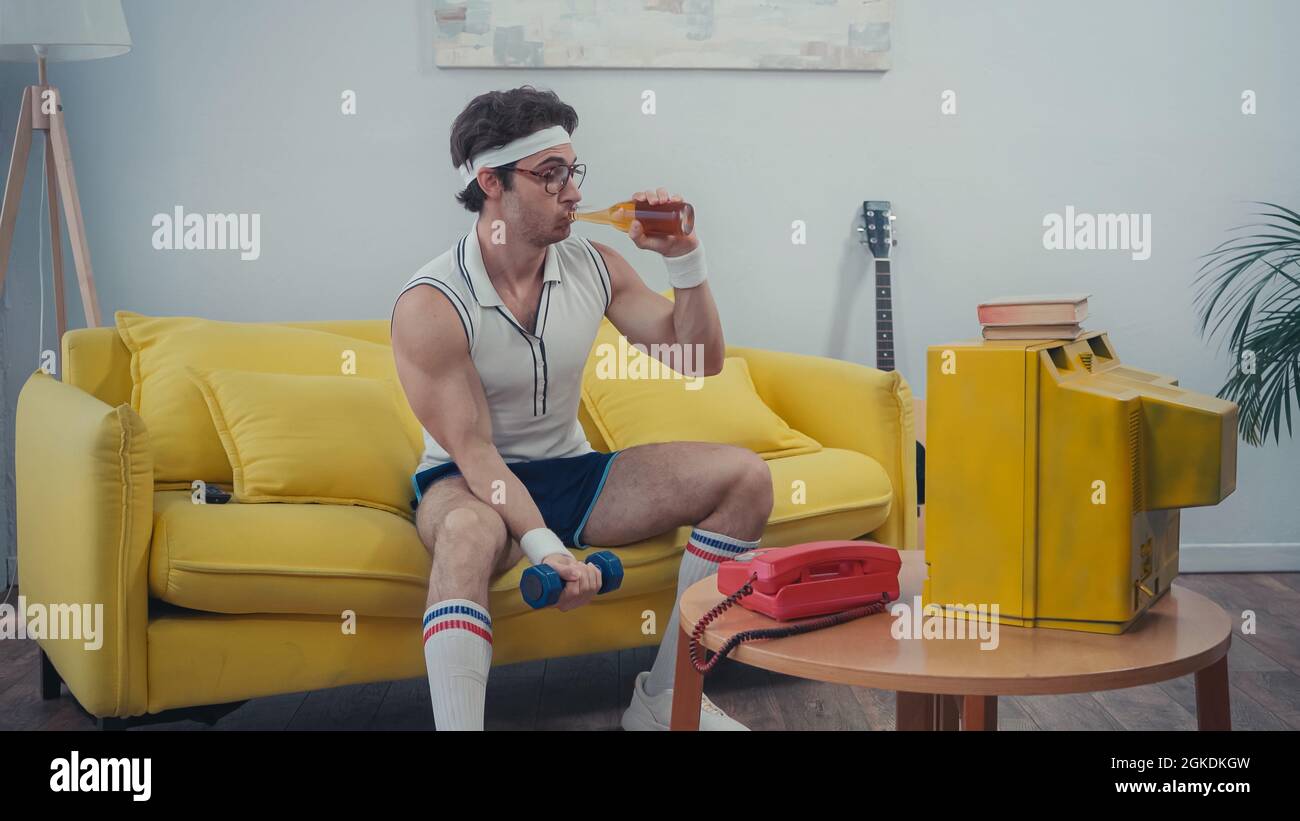 sportsman drinking beer and exercising with dumbbell while watching tv
