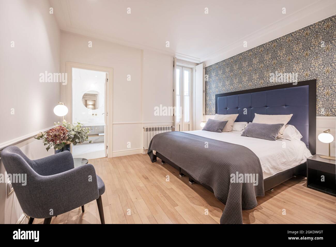 Bedroom in a vacation rental home with a king size bed, a barefoot chair and an en-suite toilet with oak flooring Stock Photo