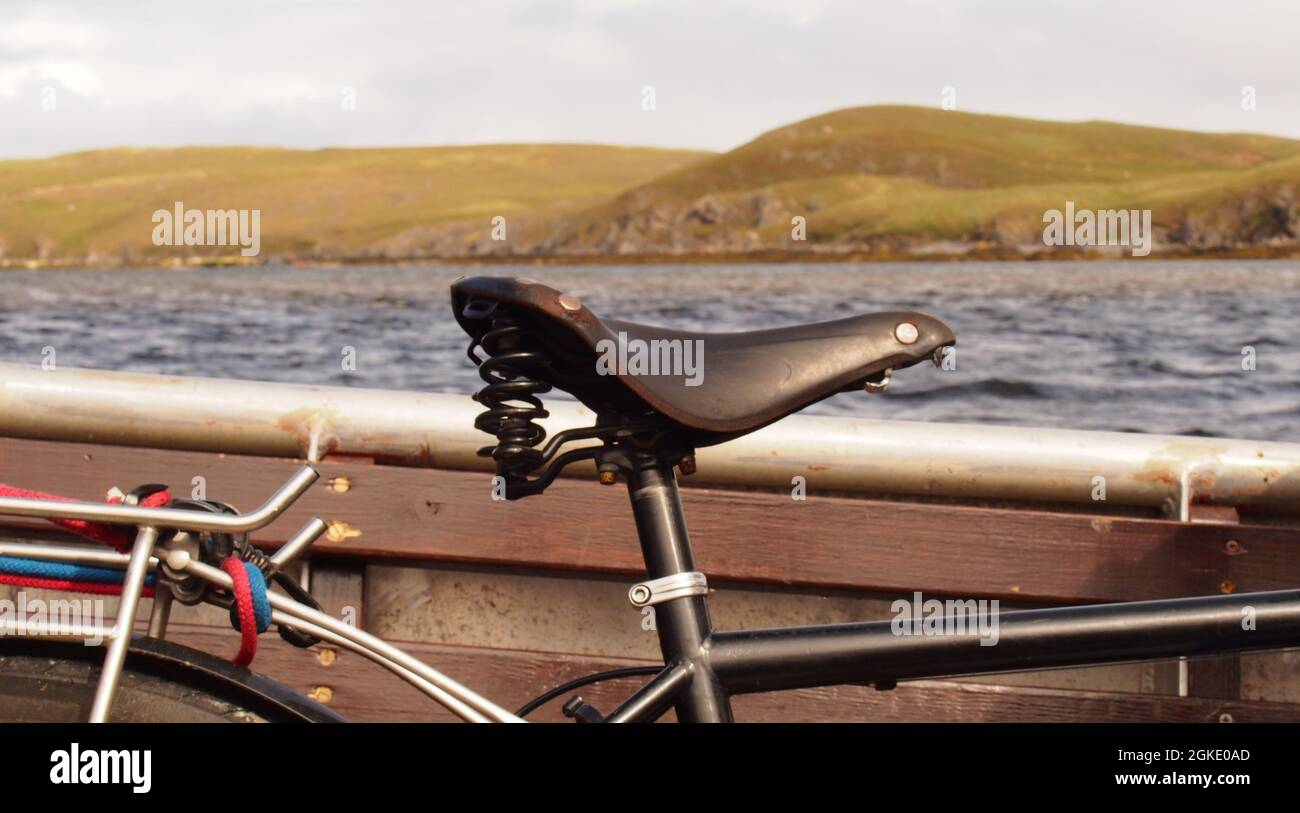 A close up view of an older, leather Brook's bicycle saddle on a pushbike aboard a small passenger ferry boat going over the Kyle of Durness, Scotland Stock Photo