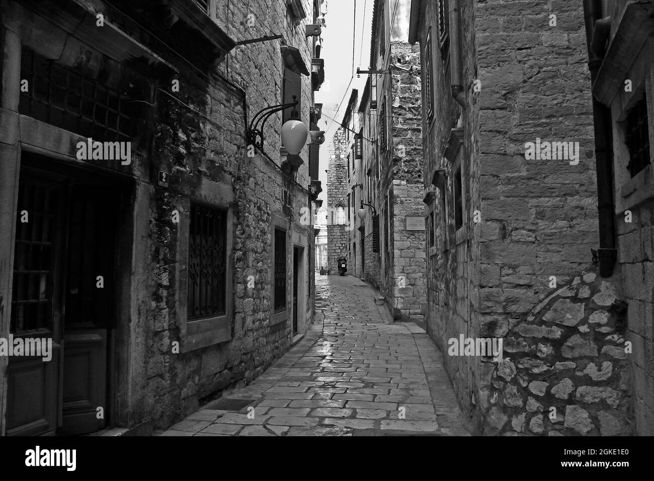 Grayscale shot of an old narrow alleyway with a cobbled street and aged ...