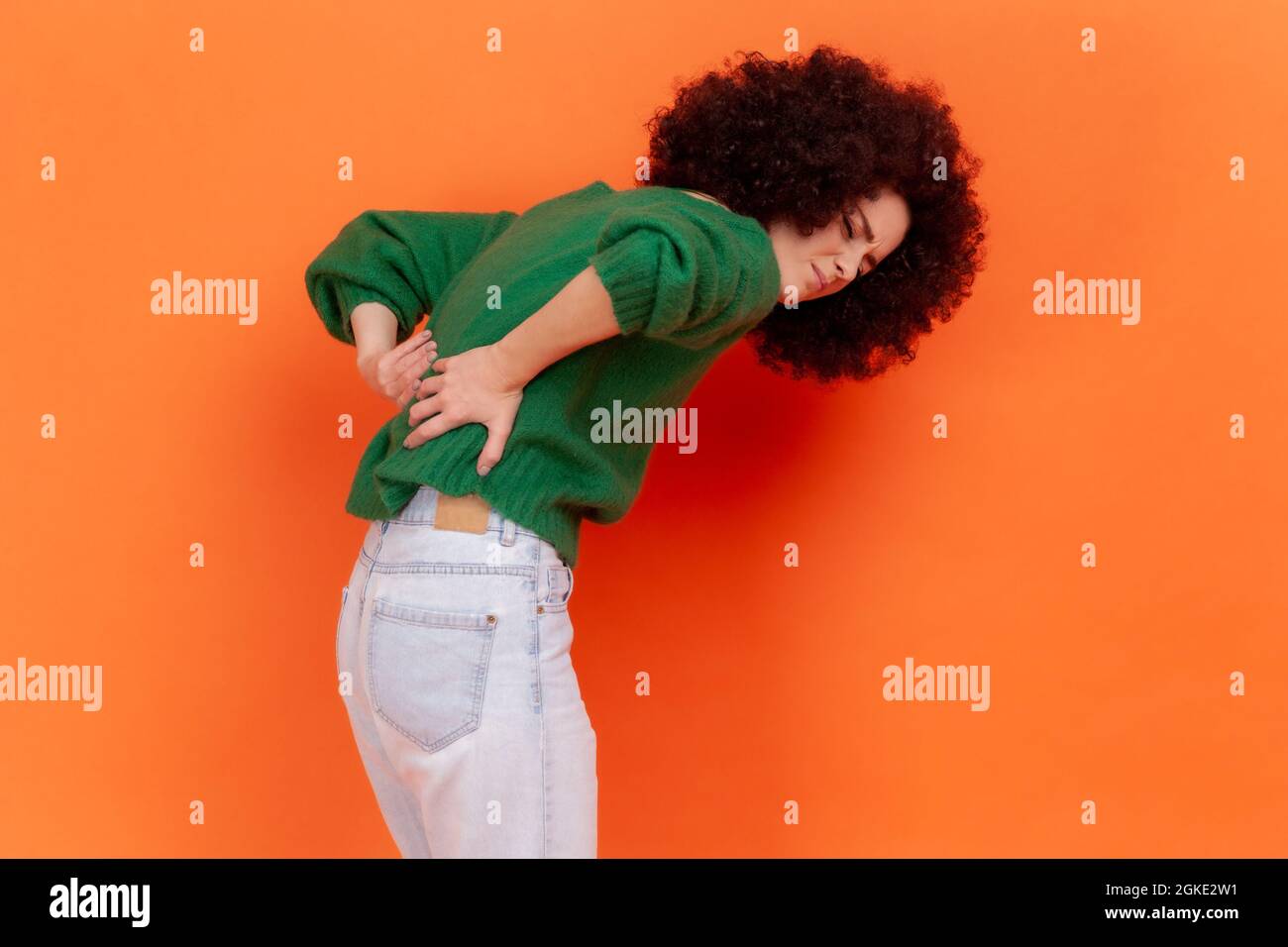 Young adult woman with Afro hairstyle wearing green casual style sweater  suffering from lower back pain, pinched nerve or kidney inflammation.  Indoor Stock Photo - Alamy