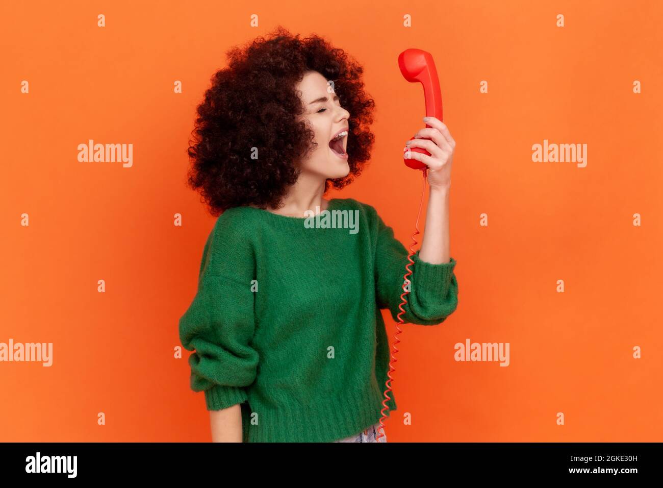 Side view of angry woman with Afro hairstyle wearing green casual style sweater screaming while talking to client in call center, negative emotions. I Stock Photo