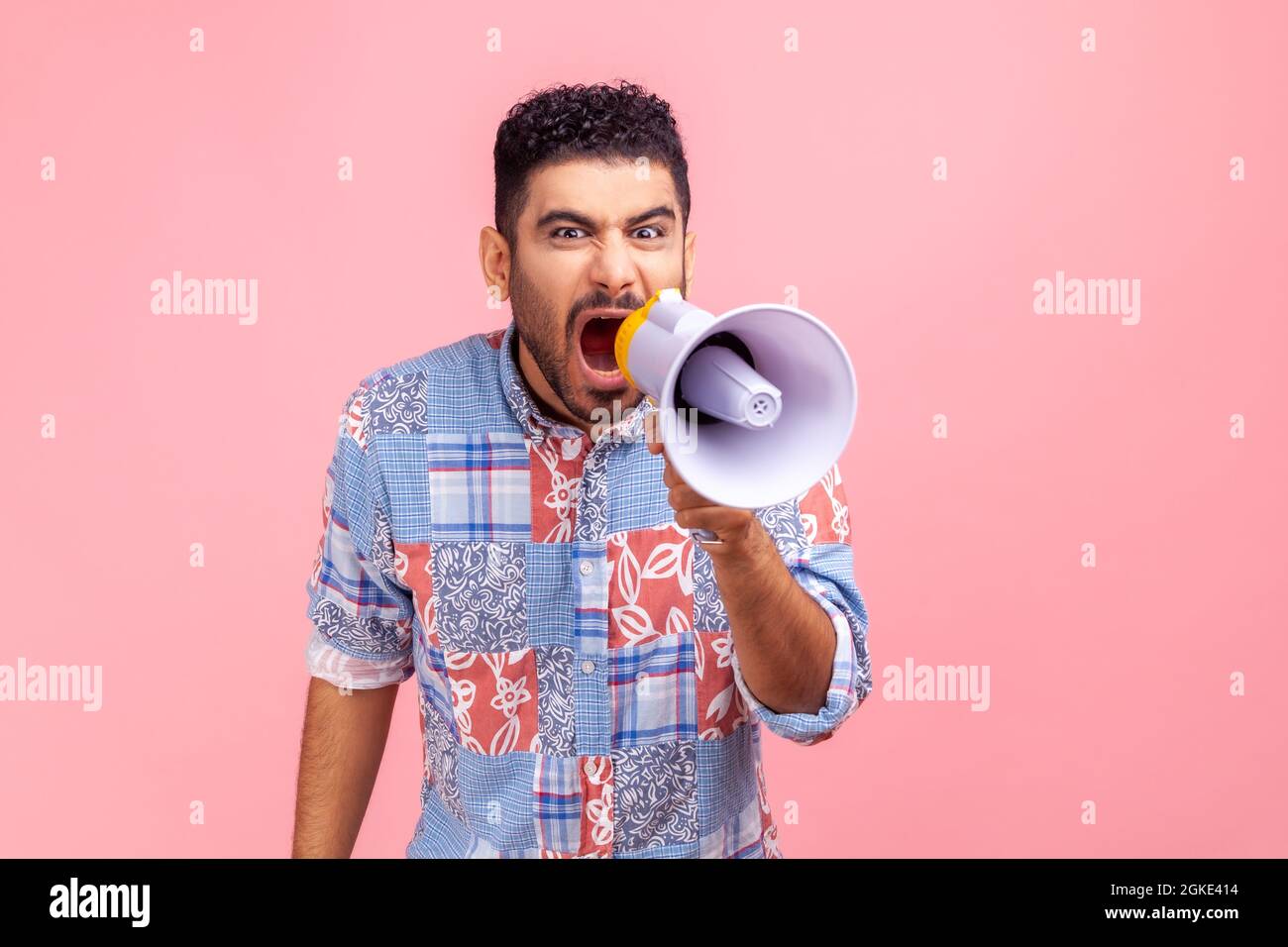 Angry man wearing casual blue shirt holding megaphone near mouth loudly speaking, screaming, making announcement, paying attention at social problems. Stock Photo