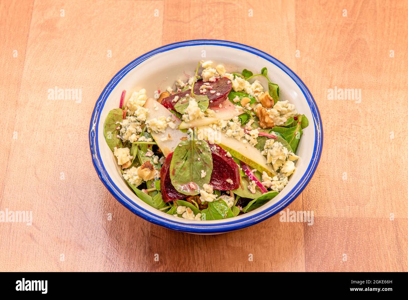 Spinach salad with beetroot slices, pear thin slices, crumbled blue cheese, pieces of nuts inside an enameled metal bowl Stock Photo