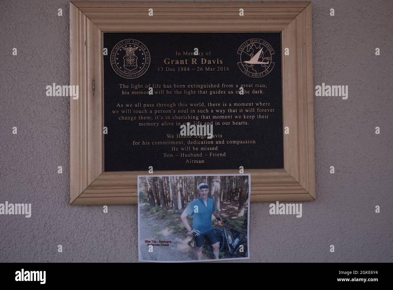 A memorial plaque for U.S Air Force Staff Sgt. Grant Davis hangs with a photo attached, outside of the 76th Airlift Squadron at Ramstein Air Base, Germany, March 26, 2021. The photo showed Davis when he rode with his father to Luxembourg and Bastogne in 2015 to pay respect to those who lost their lives in World War II. Stock Photo