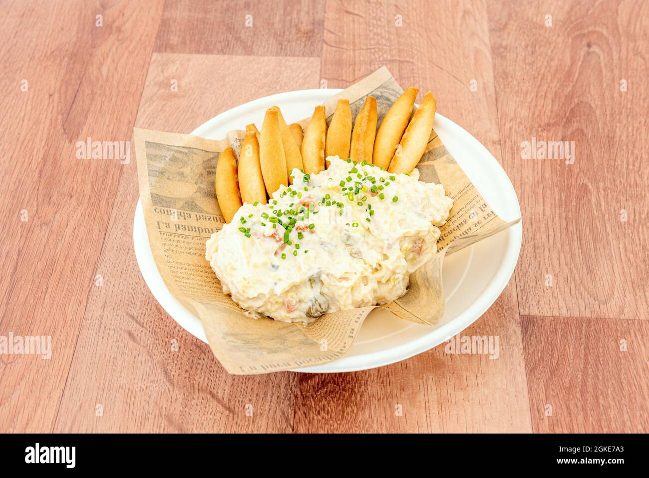 Russian salad with mayonnaise, olives, carrot, egg and boiled potatoes and a good amount of croutons to share as typical Spanish tapas on a brown tabl Stock Photo