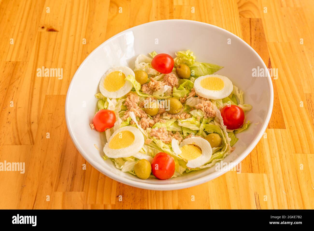 White bowl of mixed canned tuna salad with boiled egg, cherry tomatoes