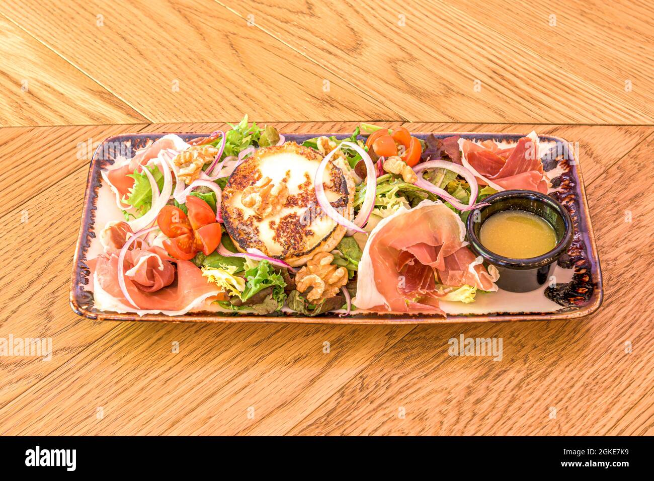 Goat cheese salad, with walnuts, slices of Serrano ham, lettuce and cherry tomatoes, red onion on porcelain tray Stock Photo