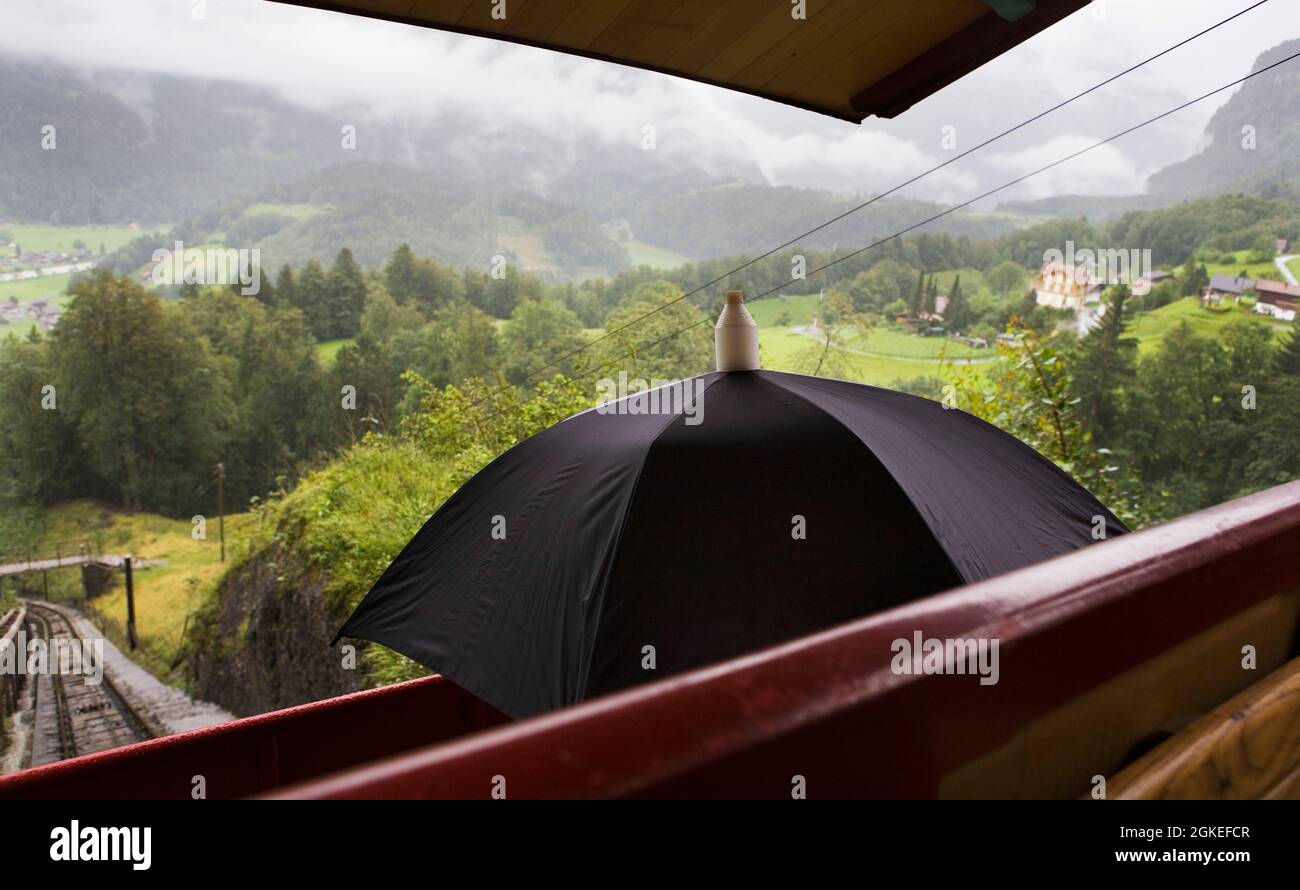 Aboard the Reichenbachfall-Bahn (the Richenbach Falls Railway), Meiringen, Switzerland: the driver uses an umbrella as a shield from the rain Stock Photo