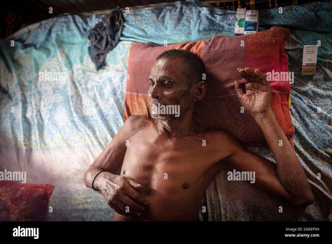 Man on his bed in his hut, next to the pillow are his medicines, he is almost blind and can only breathe with difficulty because he has been drinking Stock Photo