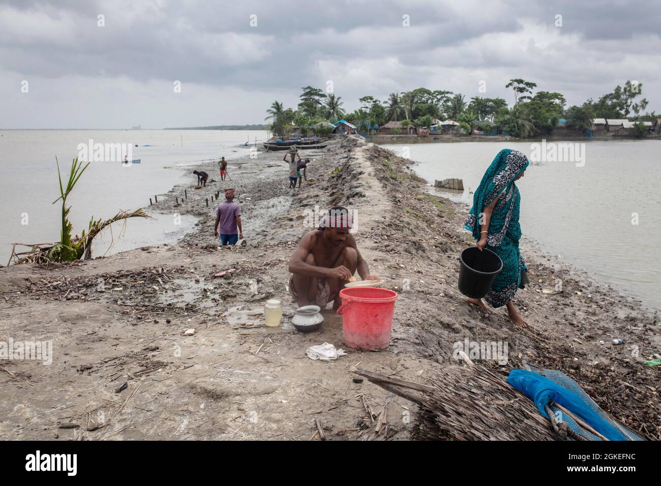 A man sieves river water from wash bowls on a muddy embankment, shrimp larvae remain in the sieve to be sold to a shrimp farm, Mongla, Sundarbans Stock Photo