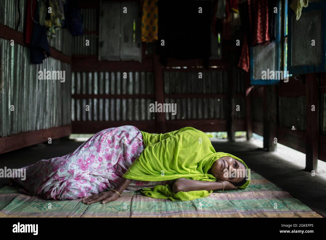 A woman lies on a carpet on the floor in her hut, contaminated drinking water made her sick, she suffers from liver cancer, Mongla, Sundarbans Stock Photo