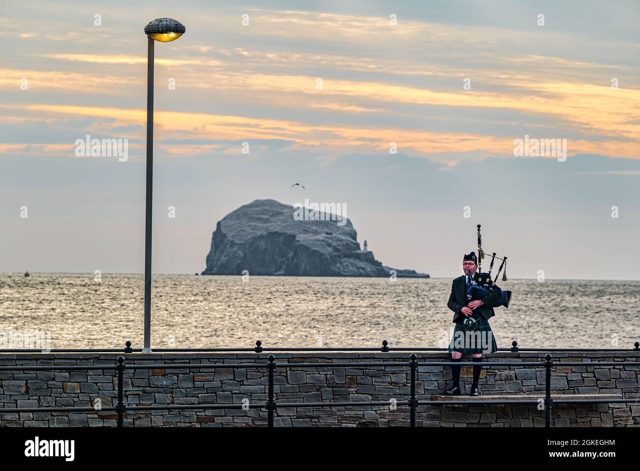 Piper plays bagpipes at dawn commemorating St Valery Day when Scottish soldiers were captured in WW II with Bass Rock, Scotland, UK Stock Photo