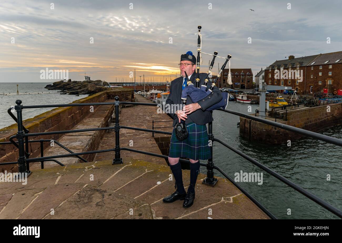 Piper plays bagpipes at dawn commemorating St Valery Day (Scottish soldiers captured in WW II) North Berwick harbour, East Lothian, Scotland, UK Stock Photo