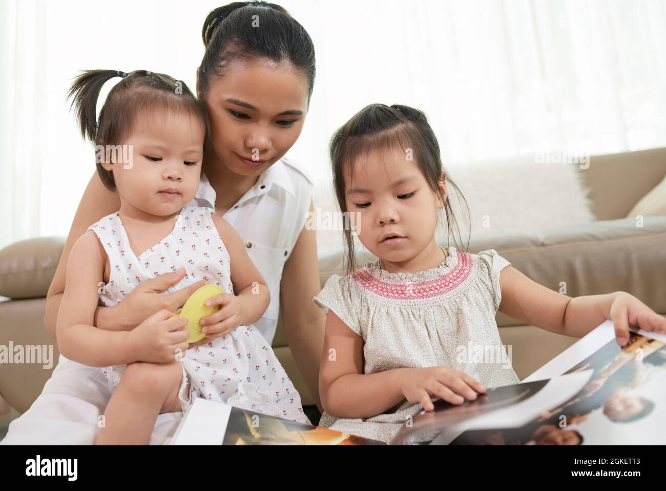 Curious little girls and their mother looking at book of printed photos Stock Photo