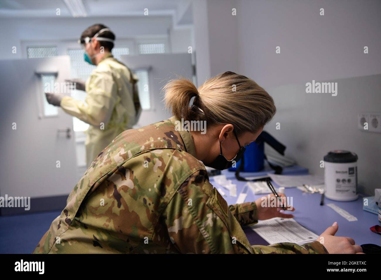 U.S. Air Force Senior Airman Kristen Nicola, 52nd Medical Group Public Health technician (front), prepares Covid test paperwork as U.S. Air Force Staff Sgt. Paul Hukreide, 52nd Medical Group Warriors Operational Health Clinic NCO in charge, prepares to administer a Covid test at Spangdahlem Air Base Germany, April 1, 2021. For Covid testing, some of the duties Public Health is responsible for is  interviewing, screening, and contact tracing patients. Stock Photo