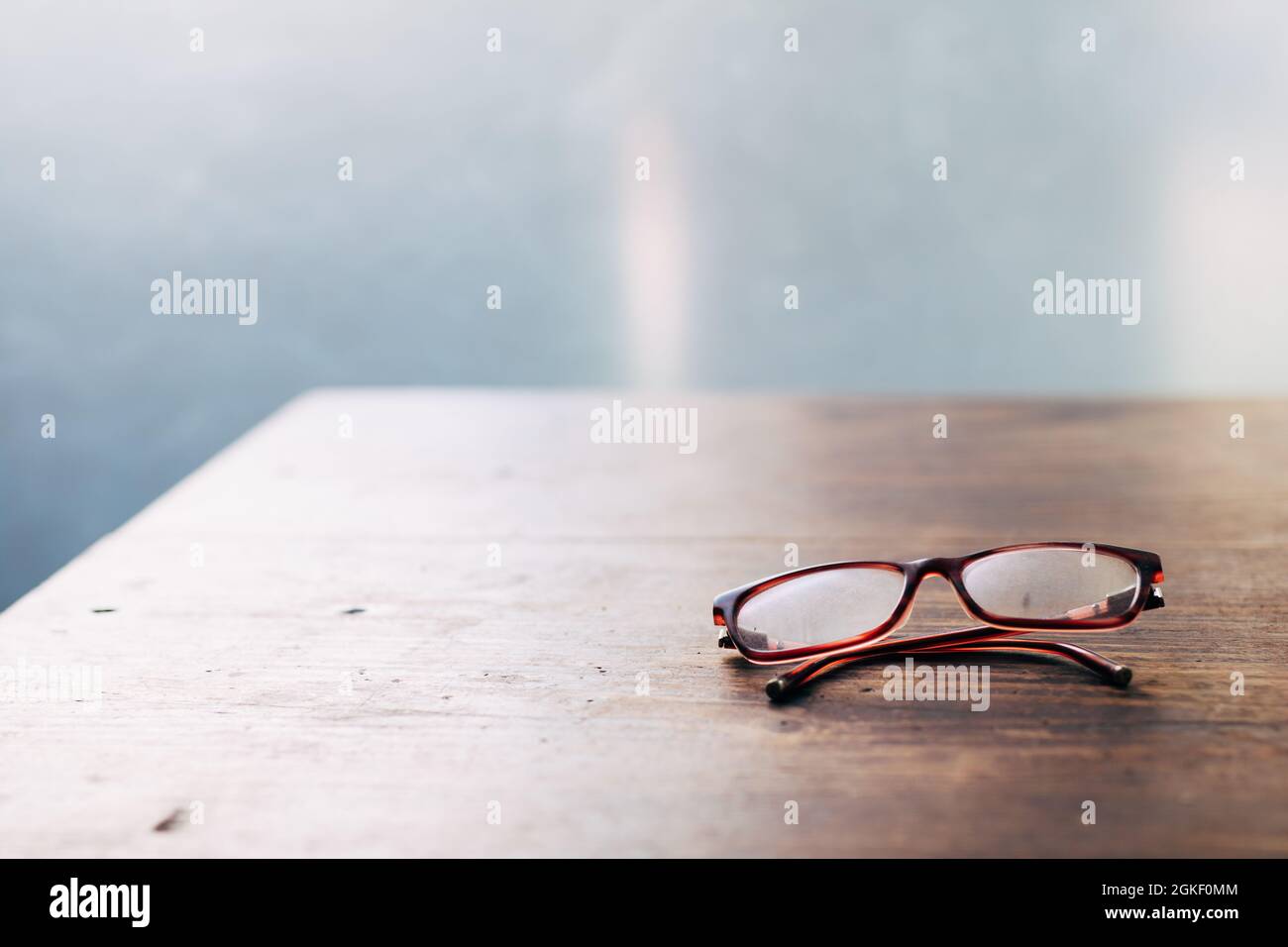 Blurred vision - Reading glasses for elderly on wooden table close-up soft focus Stock Photo