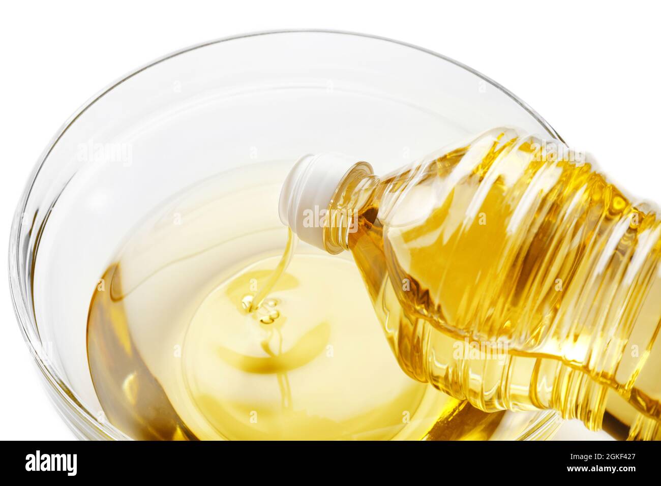 Pouring cooking oil from plastic bottle into glass bowl, on white