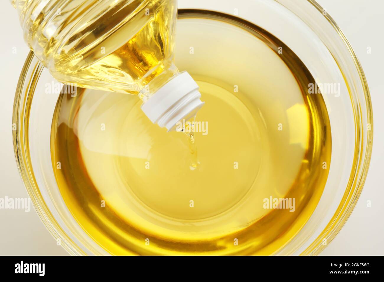 Pouring cooking oil from plastic bottle into glass bowl, closeup Stock