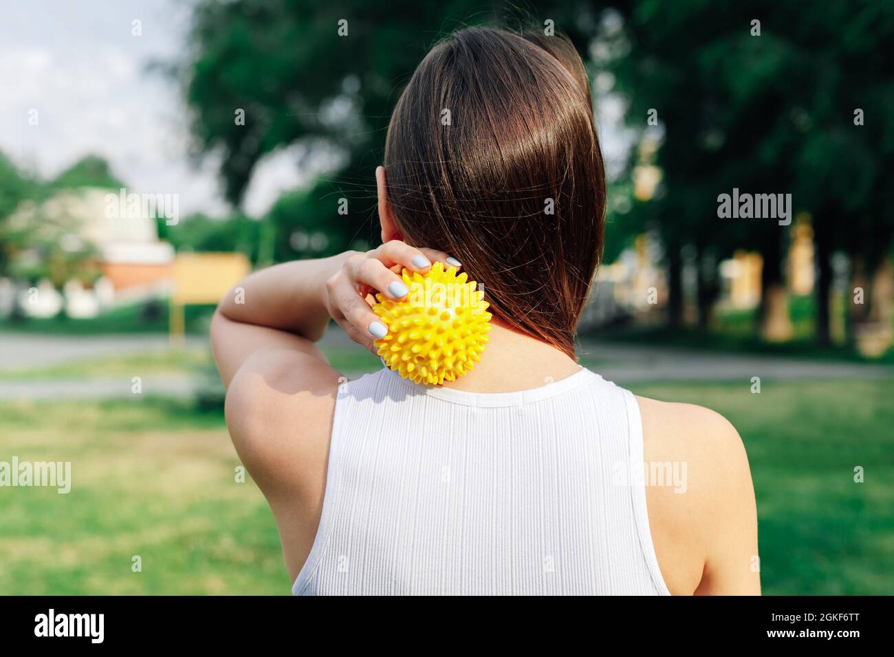 close-up on back of young woman doing neck and shoulder massage with spiky rubber ball, relaxing tense neck muscles Stock Photo