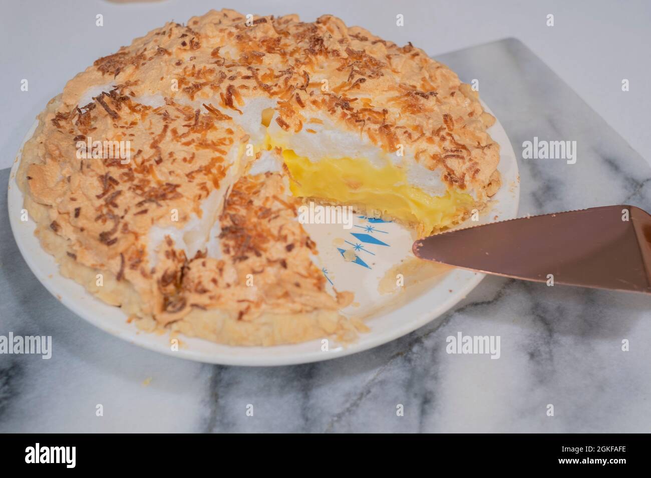 Homemade Coconut Meringue Cream pie  and serving utensil, with one slice gone, placed on a marble slab. USA. Stock Photo