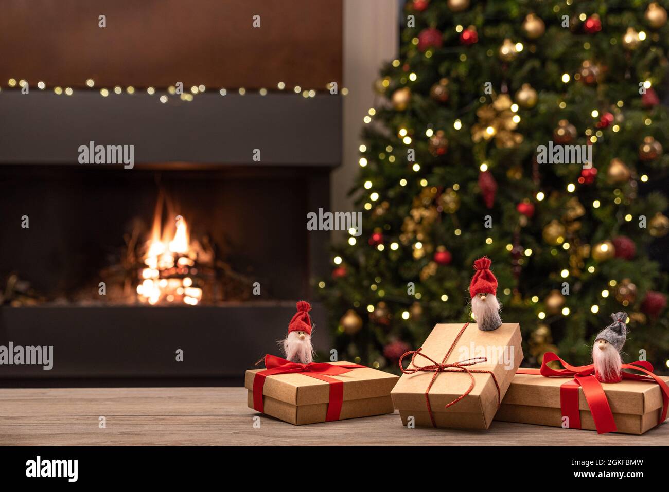 Cozy Christmas atmosphere with Christmas gnomes and gifts on wooden table in the foreground. In the background blurred the fireplace with fire, the Ch Stock Photo