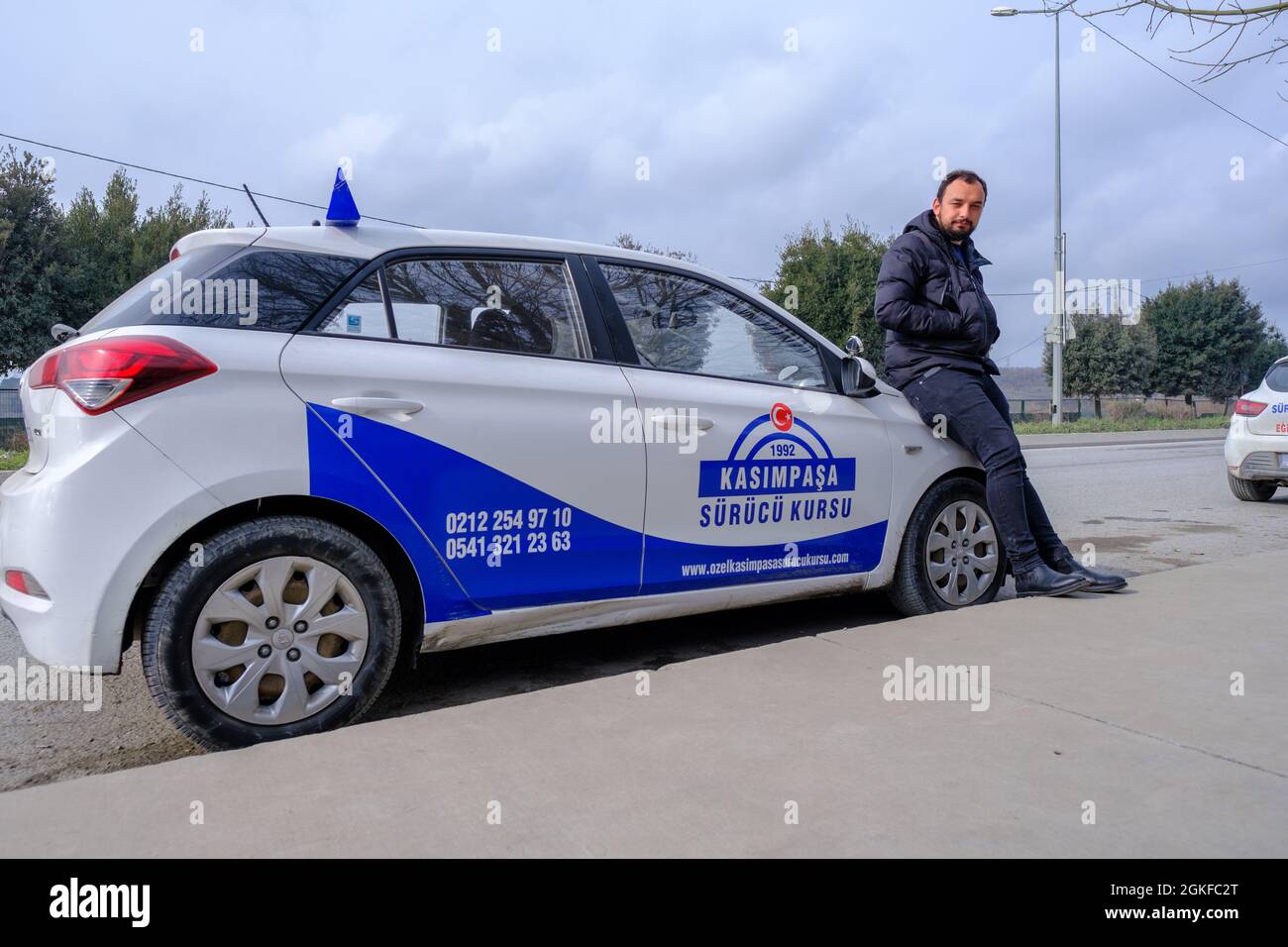 Kemerburgaz, Istanbul, Turkey - 03.19.2021: one young male instructor of driving test car in Turkey standing in front of his test car in a cloudy day. Stock Photo