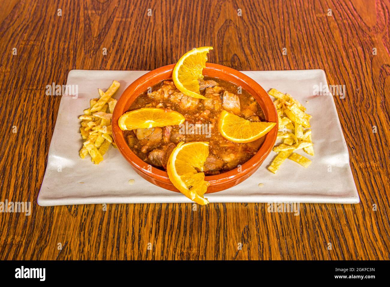 Clay pot plate with orange pork schnitzel stew and French fries on white plate Stock Photo