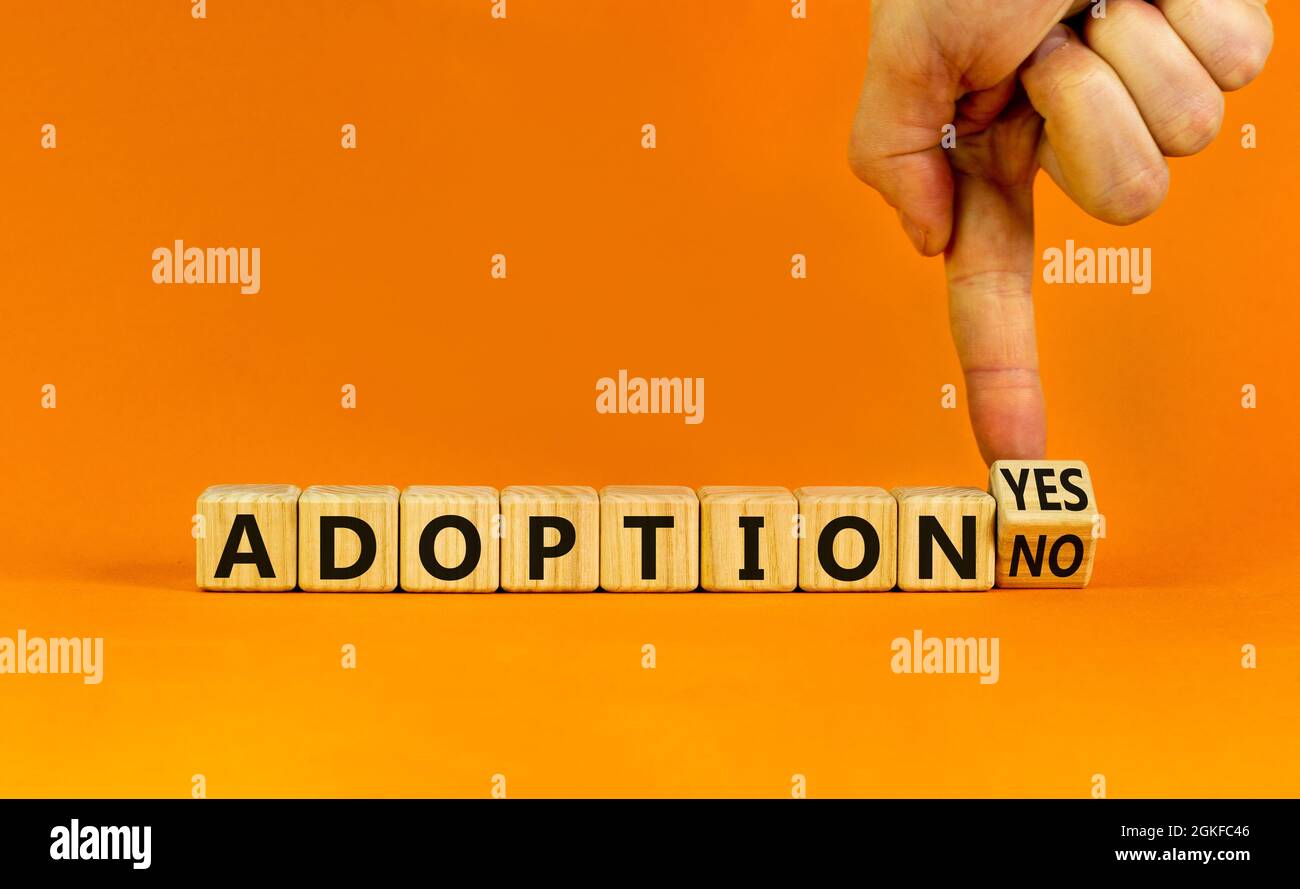 Adoption symbol. Businessman turns a wooden cube and change words 'adoption no' to 'adoption yes'. Beautiful orange background. Business and adoption Stock Photo