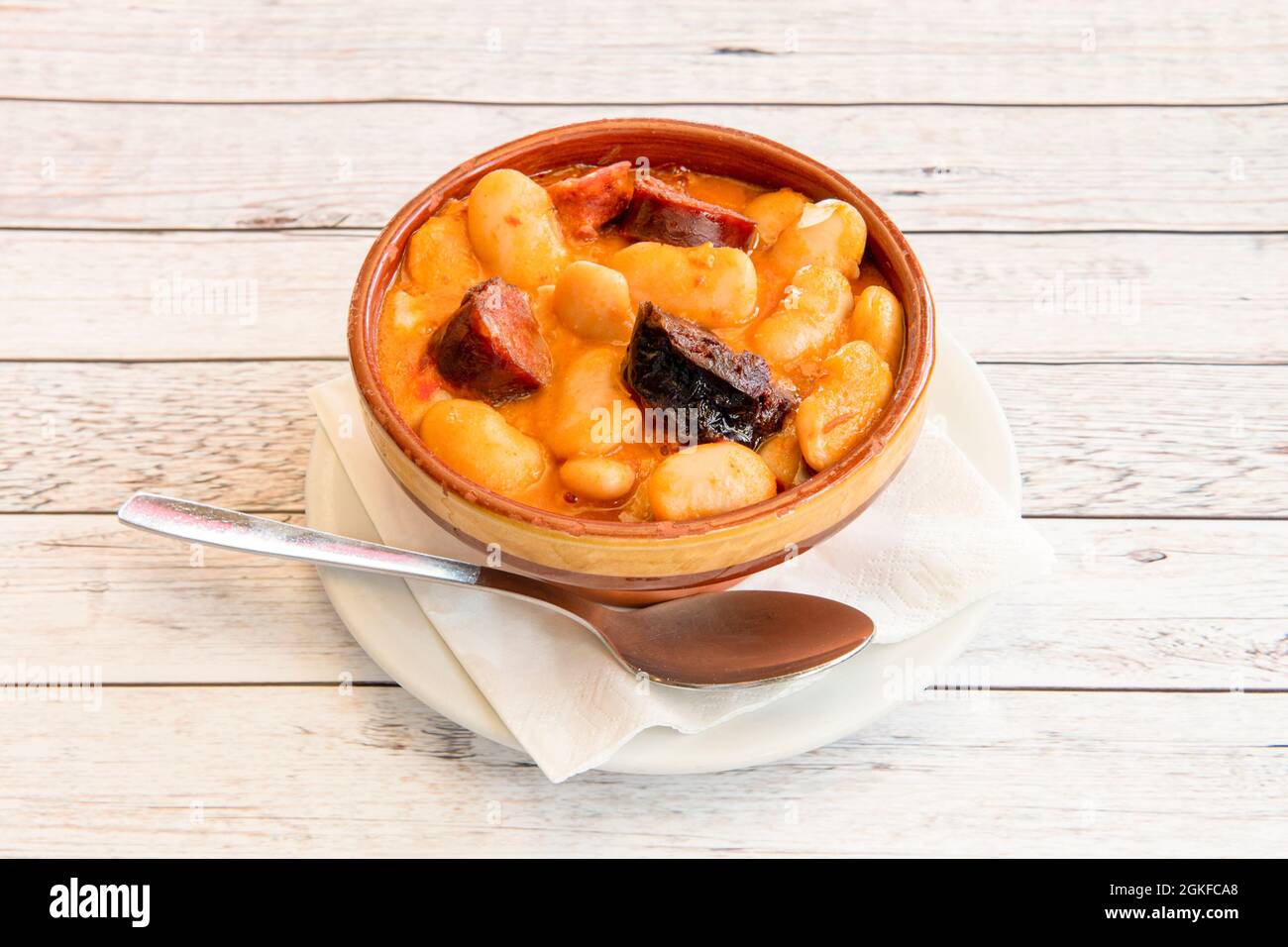 Earthenware bowl with spanish giant white bean stew recipe with pieces of cured pork, chorizo and black pudding with a spoon Stock Photo