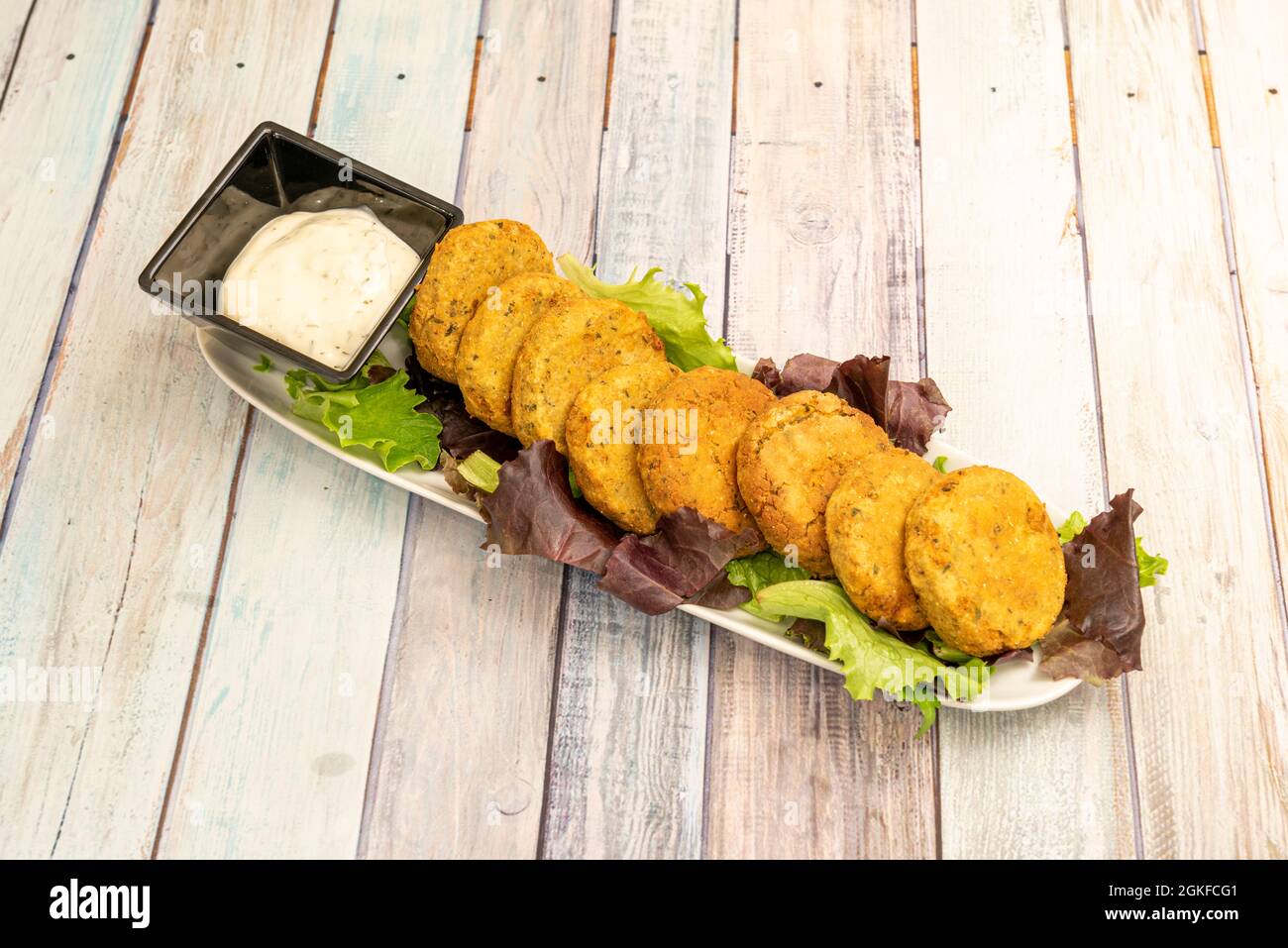 Elongated white tray filled with falafel balls on top of a bed of lettuce and accompanied by a sauce Stock Photo