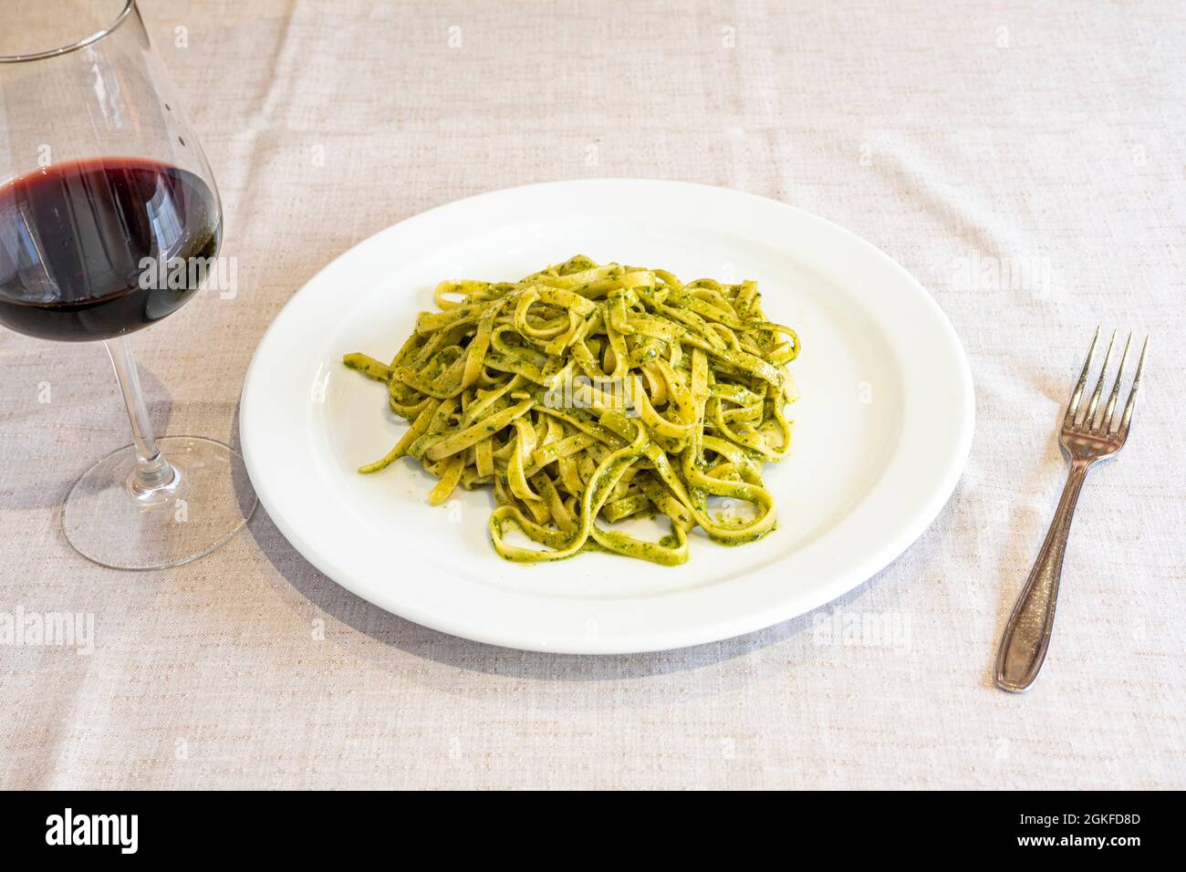 typical italian fettuccine recipe with pesto sauce on table with linen tablecloth, fork and glass of red wine Stock Photo