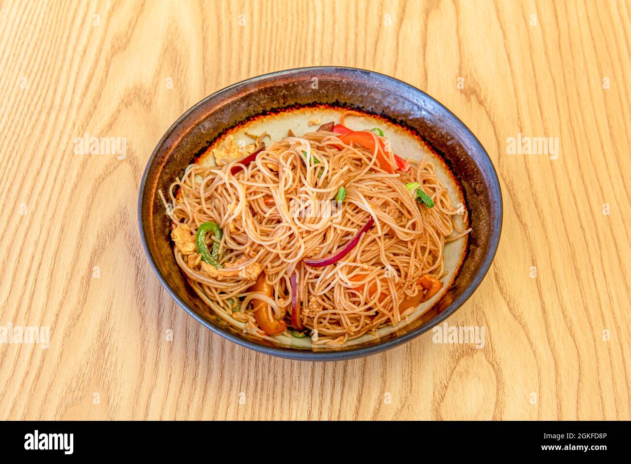 nice bowl of rice noodles with wok-sautéed vegetables, chicken pieces and  red onion on light wooden table Stock Photo - Alamy