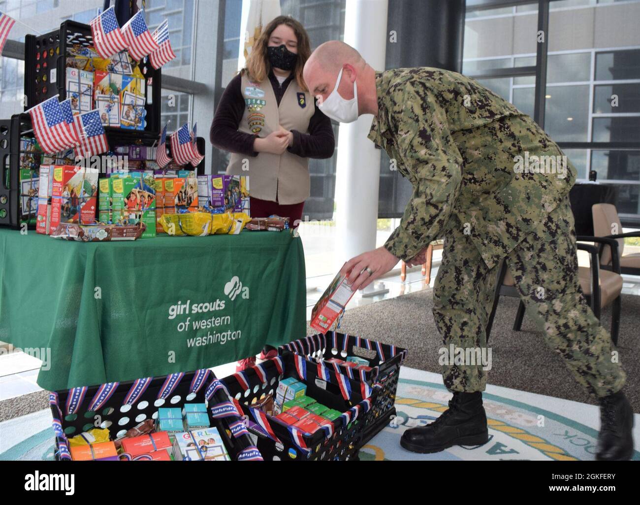 Making the tagalongs reach…For Hospital Corpsman 2nd Class Steven Pitts, the opportunity to receive a box of Girl Scout cookies a highlight. The gesture was provided by Local Girl Scout Rene Vollmuth, the daughter of Robert and Sheri L. Vollmuth, employees at Puget Sound Naval Shipyard & Intermediate Maintenance Facility , who donated 118 boxes of Girl Scout cookies to Naval Hospital Bremerton staff, April 8, 2021. The number of boxes donated was significant because Rene and her mother decided on that number to correspond for each year the naval hospital has been on land Stock Photo