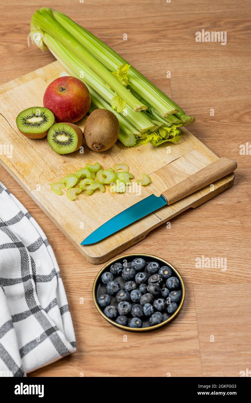 Fruits and vegetables on wooden board to prepare a detox juice. Ripe blueberries, chopped celery, kiwis, and apples. Stock Photo
