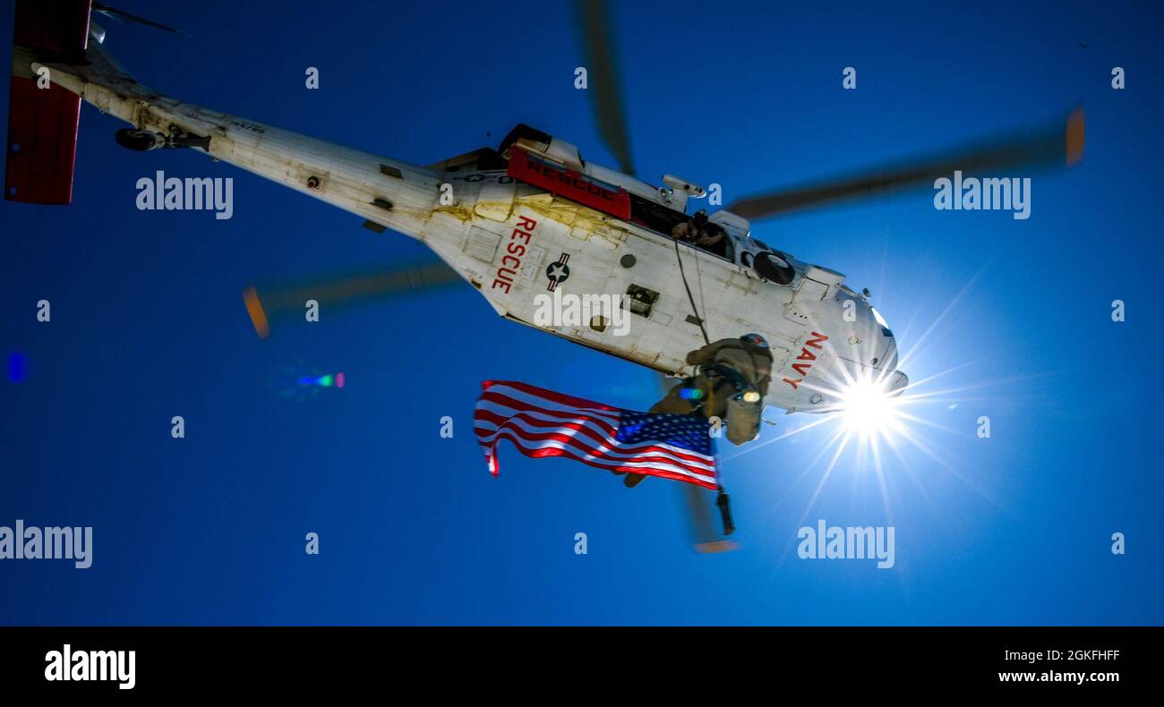 210409-N-FC670-047 FALLON, Nev. (Apr. 9, 2021)  Chief Naval Aircrewman (Helicopter) Jeffrey Roscoe, of Michigan, assigned to the “Longhorns” of Helicopter Search and Rescue (SAR) Squadron, short hauls while flying with a retirement flag during a Last Final Flight (LFF). The Navy currently has six dedicated 'Station SAR' units located around the US.  Lemoore SAR CA, Fallon SAR NV, Whidbey Island SAR WA, China Lake SAR (VX-31) CA, Pax River SAR MD, and Key West SAR FL. Their primary mission is to provide search and rescue and first responder support for Fleet flight training operations for the j Stock Photo