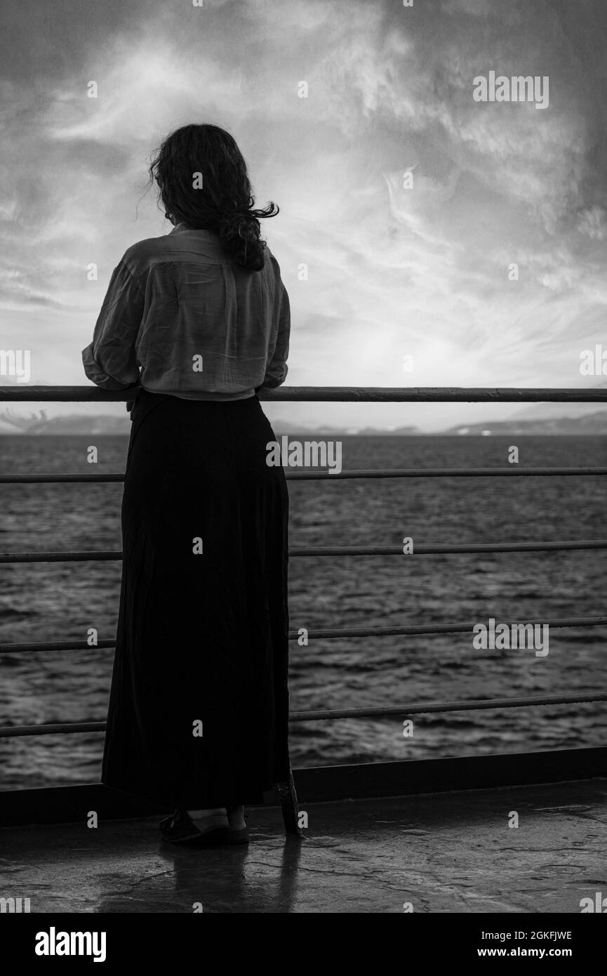 a woman's silhouette looking out to sea on the back rail of a ferry ship in the Aegean Sea Stock Photo
