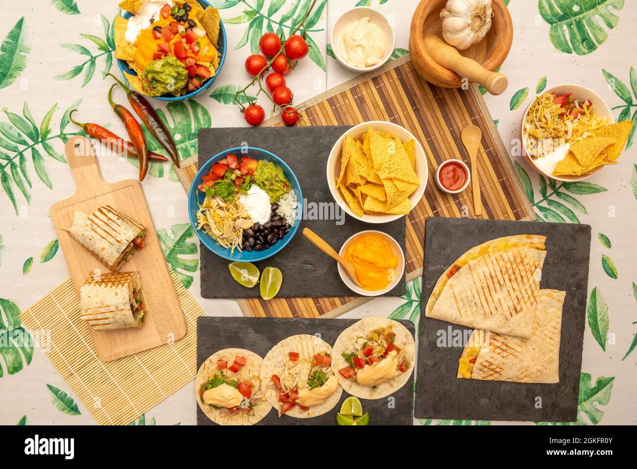 Overhead shot of popular Mexican dishes, burritos, nachos with guacamole, veal alambre, chicken tinga tacos, synchronized quesadillas, lots of lime an Stock Photo