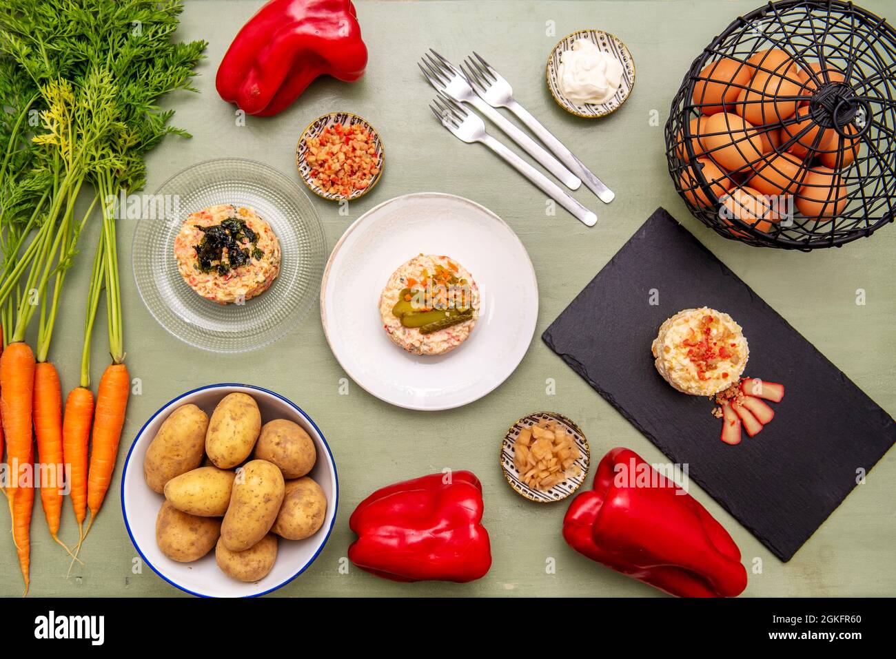 Set of assorted Russian salad dishes on green wooden table and raw ingredients Stock Photo