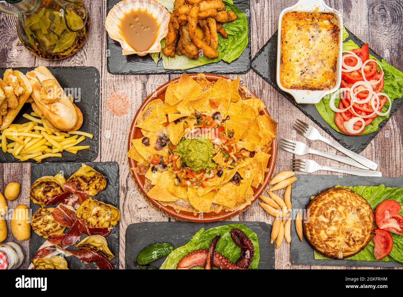 Assorted food dishes with grilled octopus, Spanish omelette, ears of bread, nachos with Mexican guacamole, artichoke flowers, parmigiana and salad Stock Photo