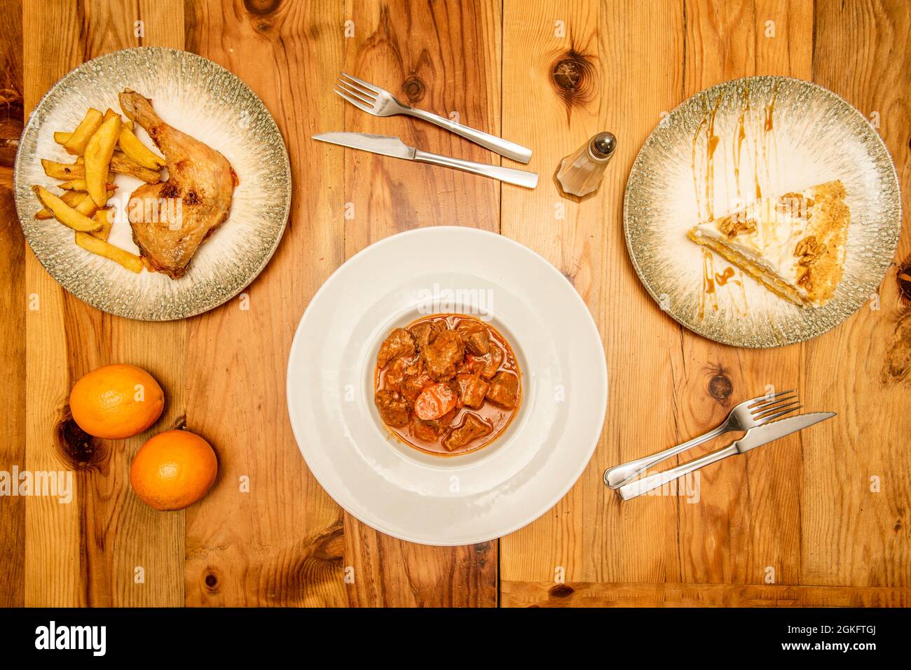 Menu for one with meat stew, roast chicken thigh with deluxe potatoes, cream pie with walnuts. Knives and forks on a pine wood table Stock Photo