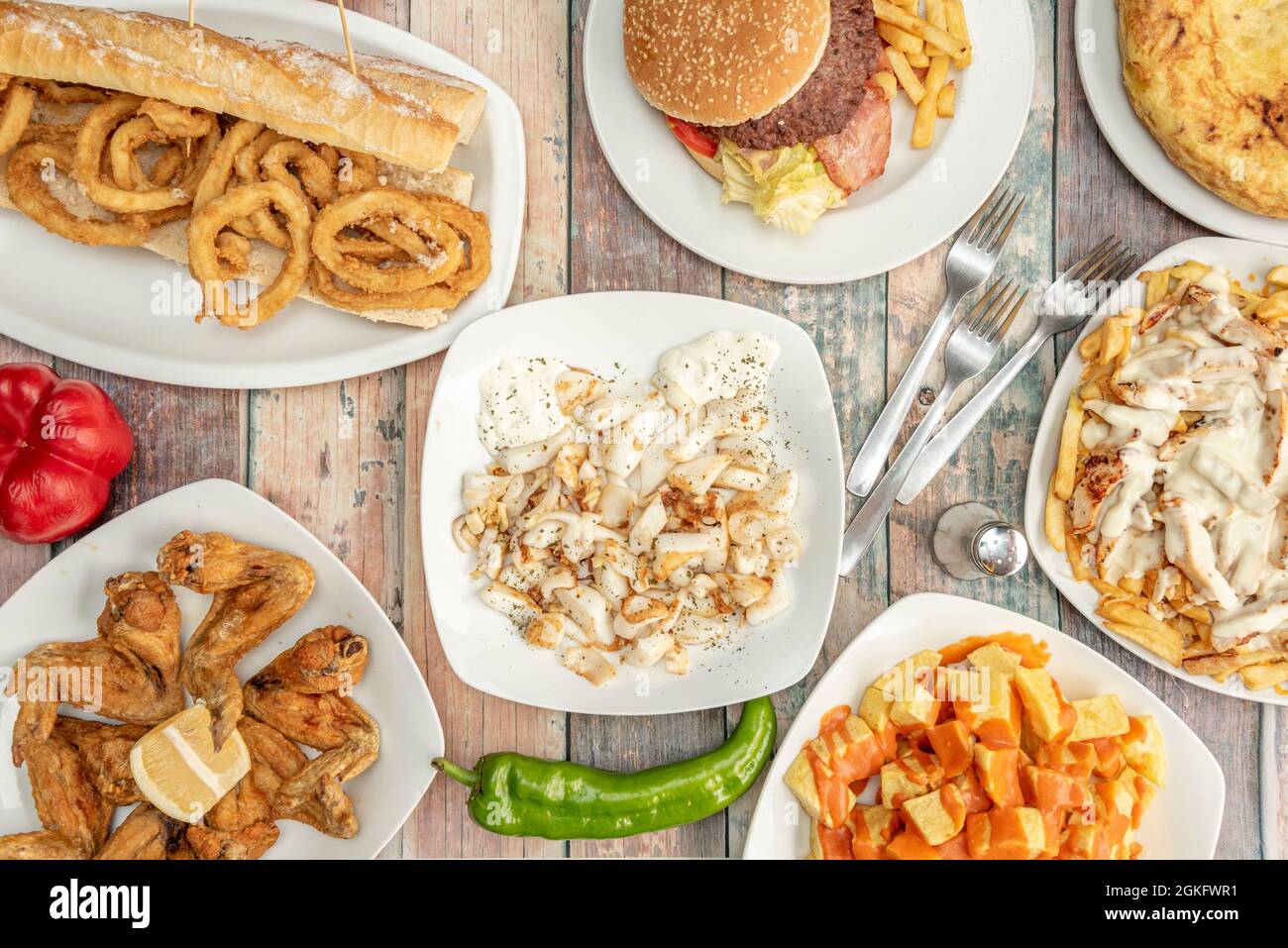 Popular tapas served in a Spanish restaurant. Patatas bravas, lemon chicken wings, squid sandwich, grilled cuttlefish with alioli, potato omelette. Stock Photo