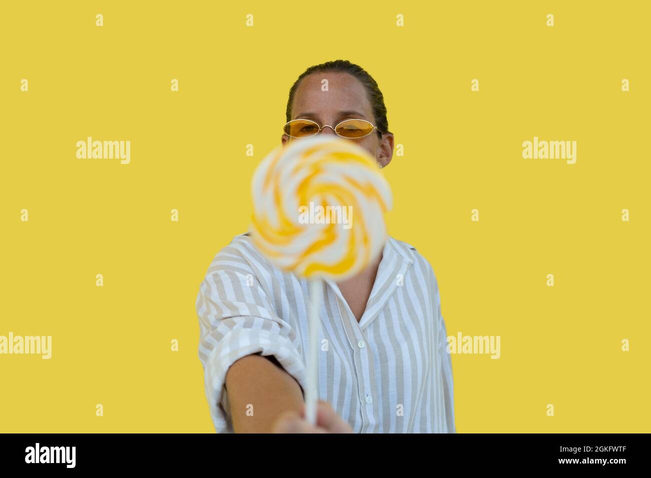 Woman in yellow sunglasses with sweet candy lollypop on yellow background Stock Photo