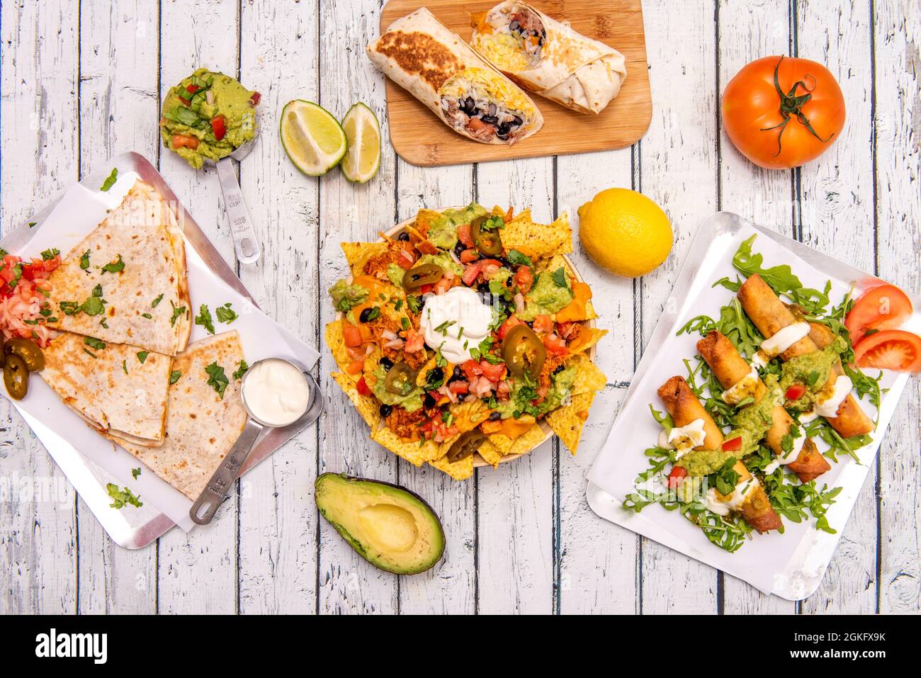 Set of popular Mexican dishes with nachos and guacamole, burritos with rice, quesadillas and golden tacos on white table Stock Photo
